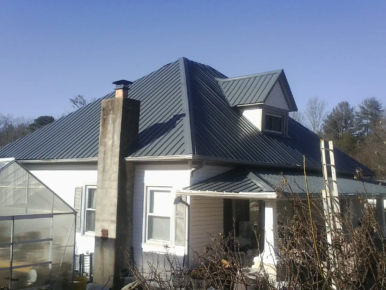 Dark blue standing seam metal roof on a white farmhouse with dormer — Slate & Tile Roof Repair by Roofing Brothers in Hanna