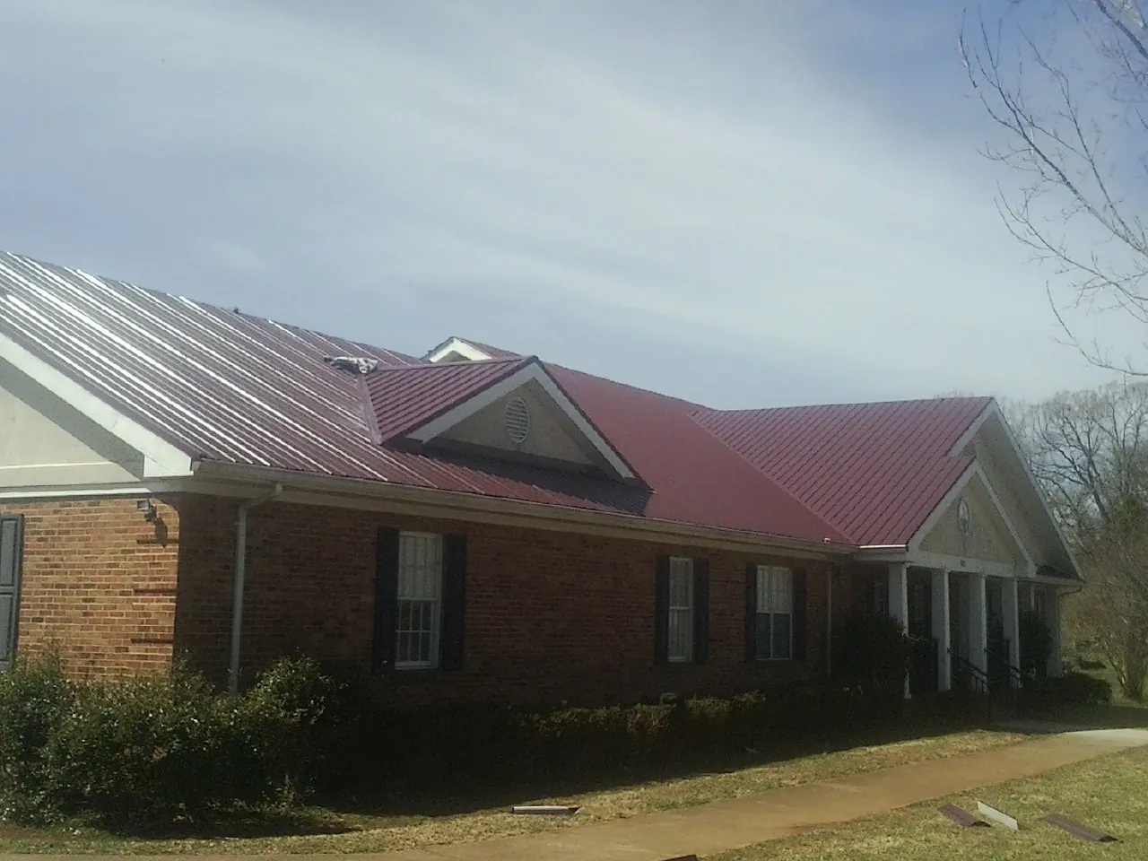 Red metal roof with gabled entries on a long brick building, from a Hail Damage Roof Repair job in Hanna