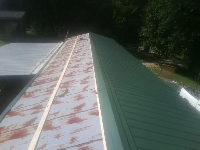 Old rusted panels beside newly installed green metal roofing — Wind Damage Roof Repair by Roofing Brothers in Hanna
