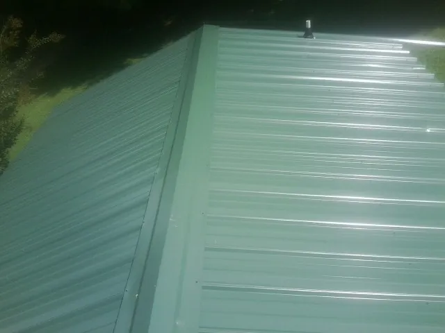 New green metal panels meeting at the ridge of a roof — Flat Roof Repair work by our crew in Hanna