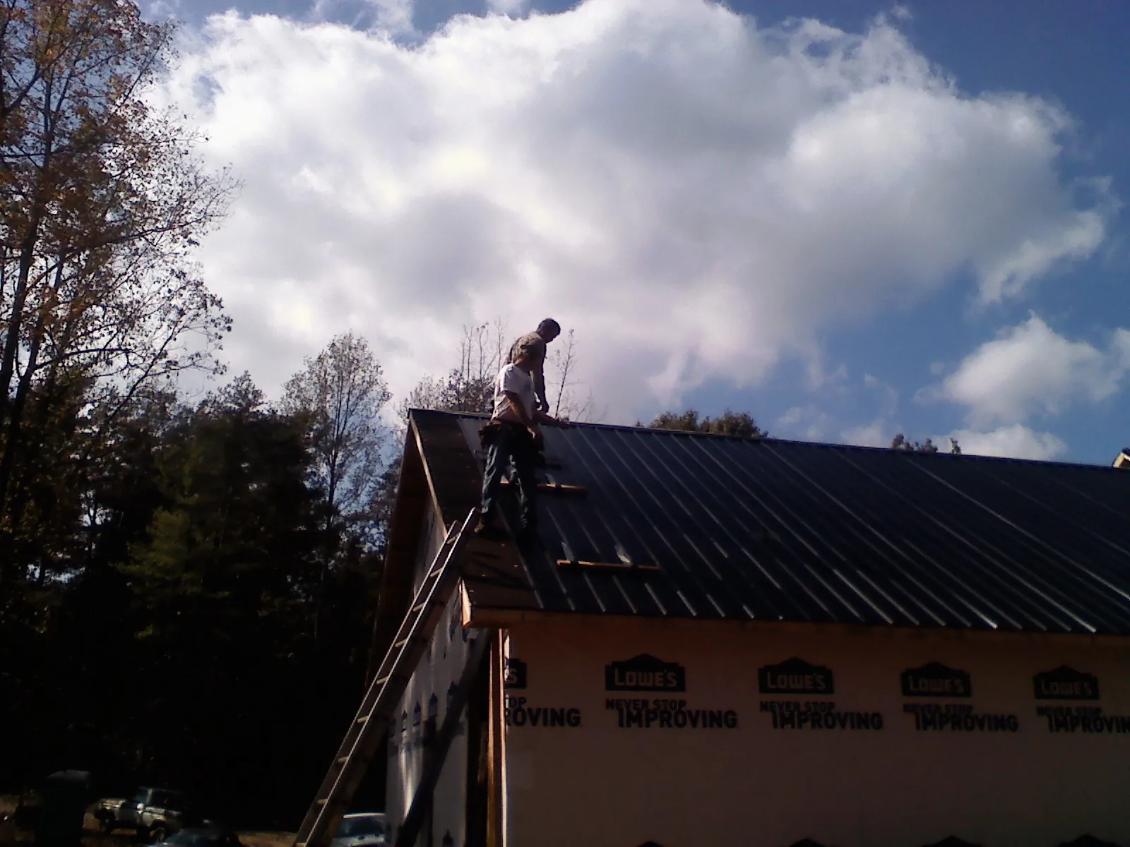Roofer fastening dark metal panels high against a cloudy sky, from a Roof Inspection job in Hanna