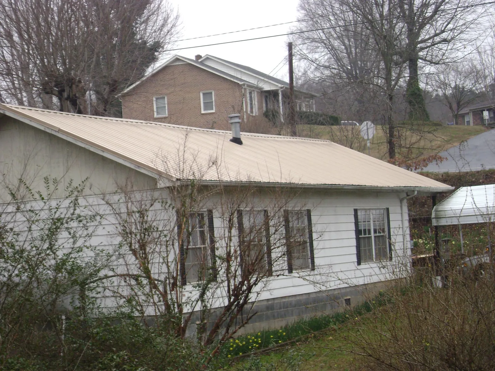 Tan metal roof on a white sided house set into a hillside — Commercial Roofing by Roofing Brothers in Hanna