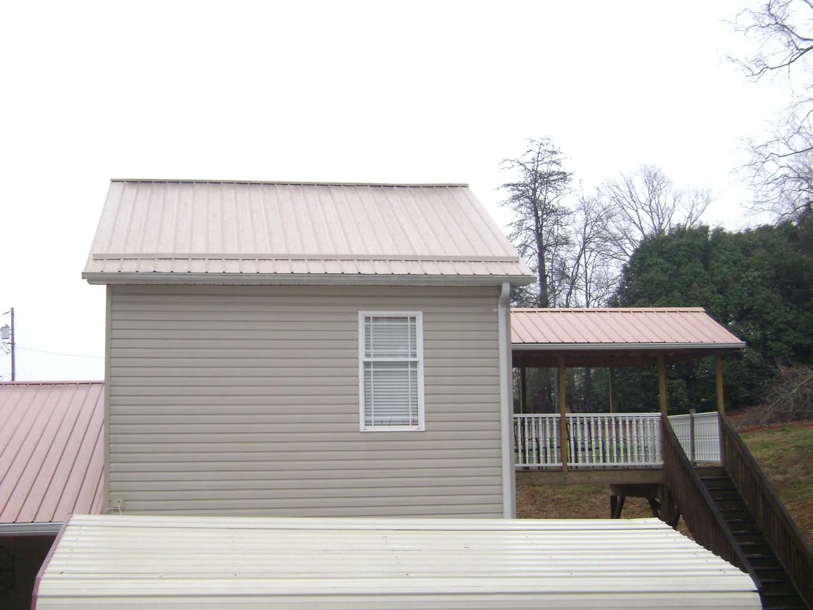 Tan metal roofs on a two story addition and attached porch, from a Roof Replacement job in Hanna