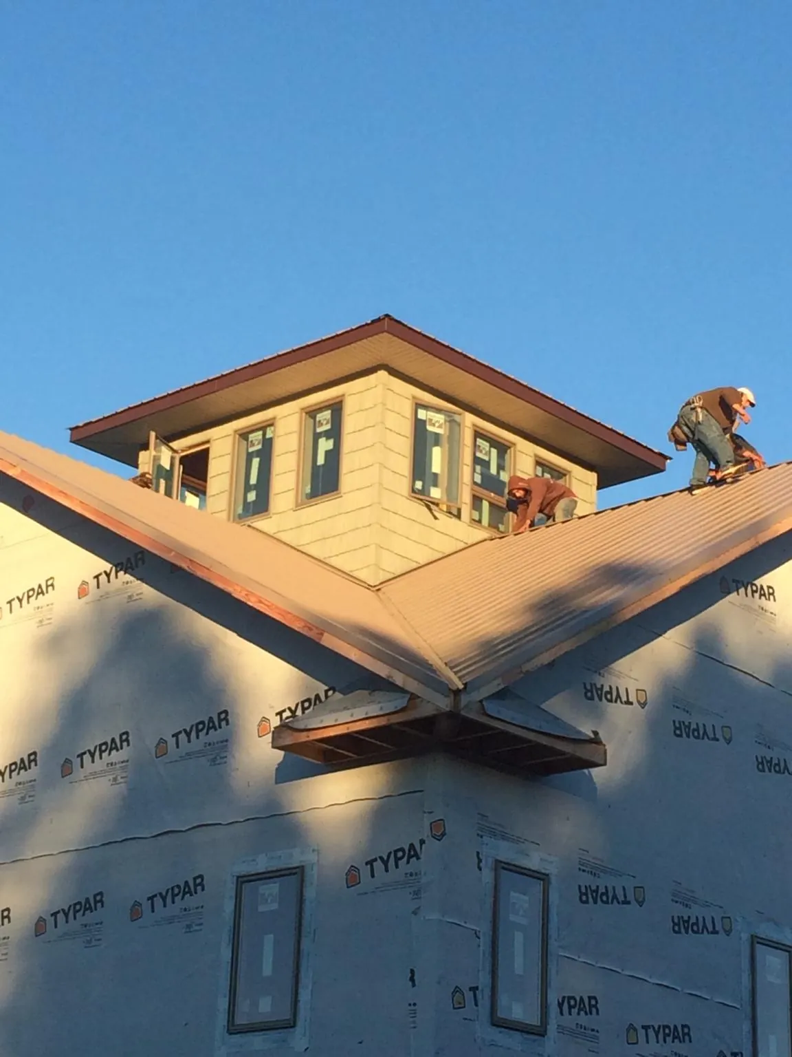 Roofers working around a rooftop cupola on a new metal roof at sunset — Roof Waterproofing in Hanna by Roofing Brothers